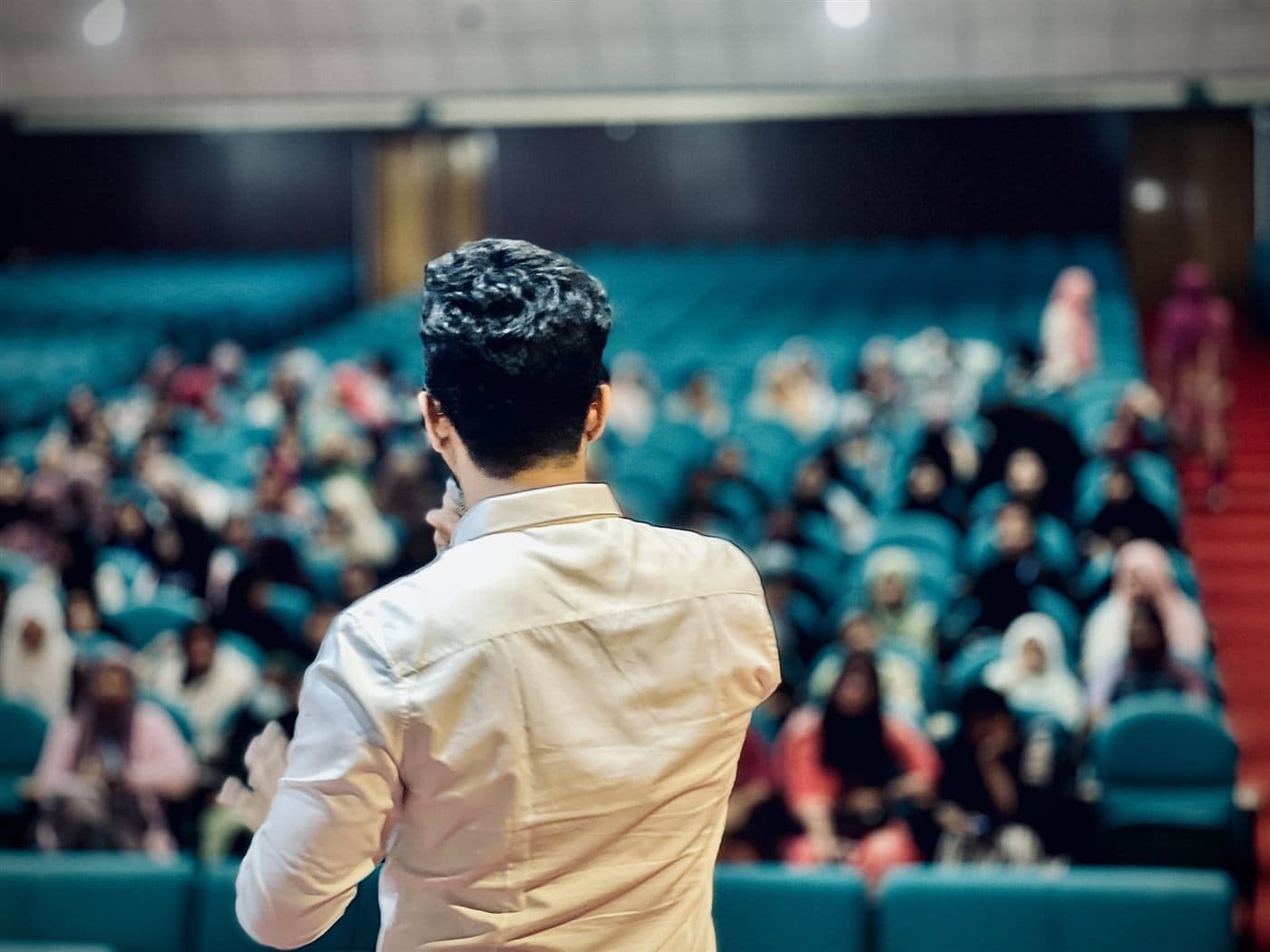 A speaker addressing a packed auditorium from the aisle
