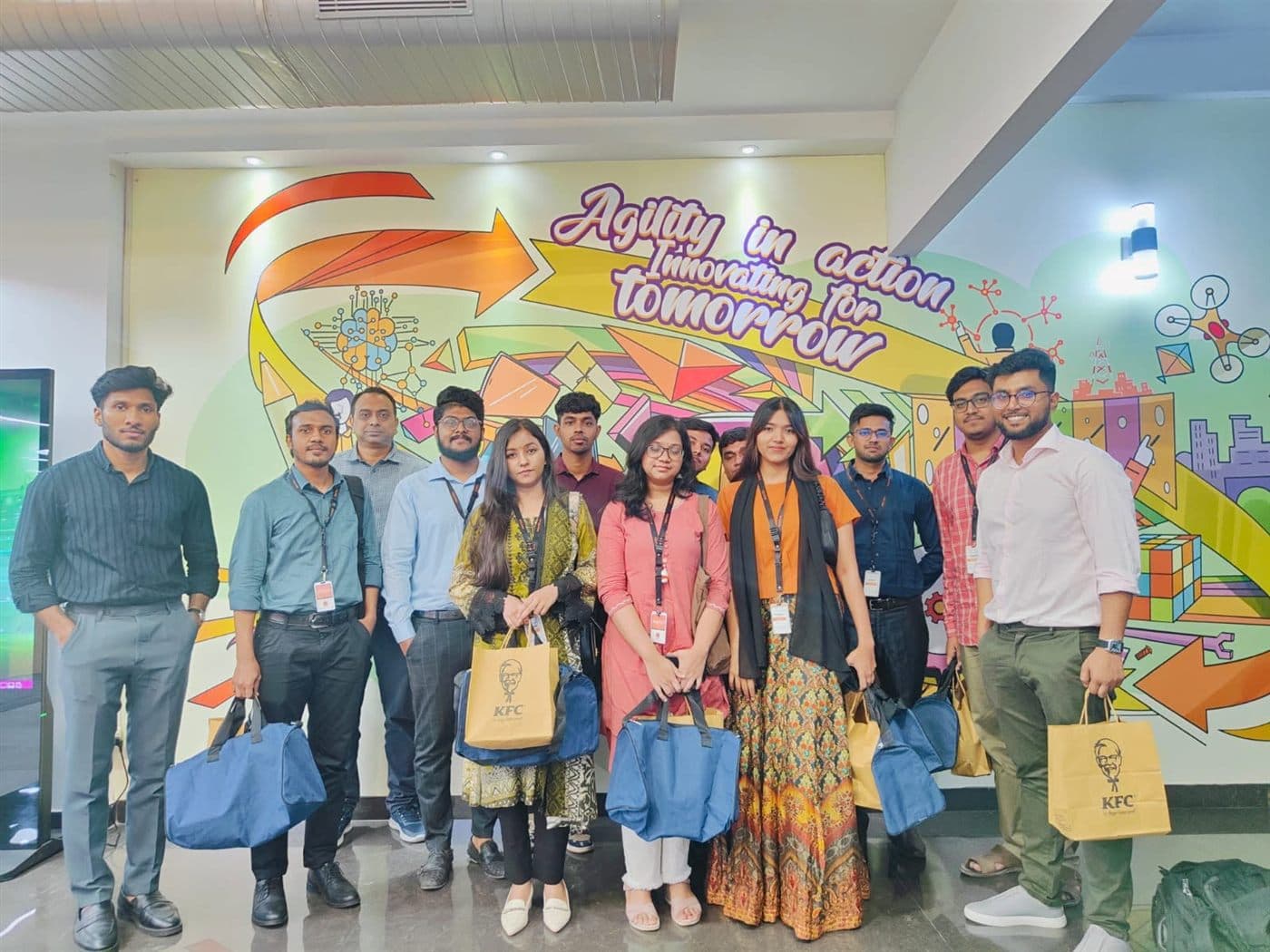 A group of visitors with lanyards in an office lobby beneath a mural reading Agility in action